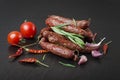 Smoked sausage with rosemary, pepper, tomatoes and garlic on a black background. Royalty Free Stock Photo