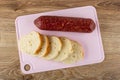 Smoked sausage and slices of bread on cutting board on wooden table. Top view Royalty Free Stock Photo