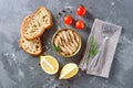 Smoked sprat with oil in an open tin can, whole grain bread, lemon, fresh tomatoes on a concrete background Royalty Free Stock Photo