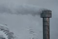 Smokestack with Smoke column and snow covered mountains