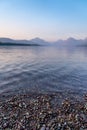 Smokey hazy view of Lake McDonald at sunset in Glacier National Park. Pebbles in foreground in selective focus Royalty Free Stock Photo