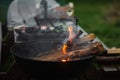 The smoking brazier of a round form. Firewood flares up in the brazier against the background of green grass. The concept of