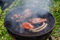 Smoking charcoal grill with open lid. Grill grate with steaks, sausages, vegetable skewers.