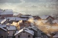 Smoking chimneys at roofs with snow of houses emits smoke, smog at sunrise, pollutants enter atmosphere. Environmental disaster. Royalty Free Stock Photo