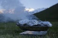 Smoking outside portable grill, mountains and grass in the background. Moment stopped