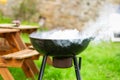 A smoking round grill on a background of green grass. Preparing for a picnic