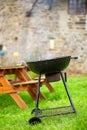 A smoking round grill on the background of wooden tables with benches. Preparing for an outdoor picnic