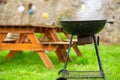 A smoking round grill on the background of wooden tables with benches. Preparing for an outdoor picnic