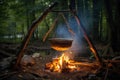 smoldering campfire with goulash pot hanging from a tripod