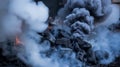 A smoldering pile of charcoal emits thick smoke and a small flame in the dark Royalty Free Stock Photo