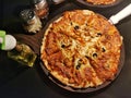 Smooth baked thin crust pizza on wooden plate. Olive oil, oregano and chili flakes on the side Royalty Free Stock Photo