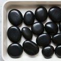 Smooth, black spa stones are arranged neatly in a white rectangular tray. Each stone Royalty Free Stock Photo