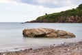 Smooth, calm sea around a shoreline rock at St Mary`s Bay beach in Torbay, Devon, with some coastline cliffs in the background