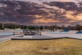 A smooth concrete skatepark surrounded by yellow winter grass, green umbrellas over benches, bare winter trees