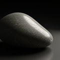 Smooth, dark grey pebble with subtle veins, set against a gradient black and grey Royalty Free Stock Photo