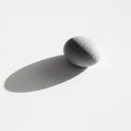 A smooth, grey, oval-shaped stone on a white surface casts a distinct shadow Royalty Free Stock Photo