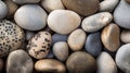 Smooth, multicolored pebbles in shades of gray, beige, and brown, some with black spots, arranged closely together