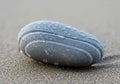 Smooth, oval-shaped gray stone lying on fine sandy surface. The stone\'s texture is polished with Royalty Free Stock Photo