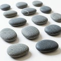Smooth, oval-shaped grey stones are arranged on a white surface. The stones have a Royalty Free Stock Photo
