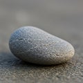 Smooth, oval-shaped pebble with a subtle gray hue rests on a textured sandy surface. Royalty Free Stock Photo