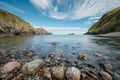 Smooth pebbles line the tranquil waters of a bay, surrounded by dramatic cliffs and a Royalty Free Stock Photo