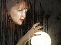 Smooth portrait of female model, posing behind transparent glass covered by water drops. woman holding large glowing