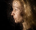 Smooth portrait of model, posing behind transparent glass covered by water drops. young melancholy and sad woman Royalty Free Stock Photo