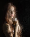 Smooth portrait of model, posing behind transparent glass covered by water drops. young woman holding a glass of Royalty Free Stock Photo