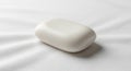 A smooth, rectangular bar of white soap with rounded edges rests on a white fabric Royalty Free Stock Photo