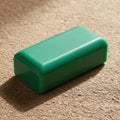 A smooth rectangular solid green object with rounded edges sits on a textured surface isolated on white background Royalty Free Stock Photo