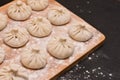 Smooth rows of raw khinkali crushed by flour lying on the corner of a wooden board