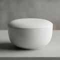 A smooth, white ceramic bowl with a lid is centered on a neutral gray surface. The bow Royalty Free Stock Photo