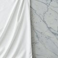 Smooth white fabric draped elegantly on the left side, contrasting with a grey marble Royalty Free Stock Photo