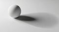 A smooth, white spherical object rests on a flat, light surface. It casts a long, soft Royalty Free Stock Photo