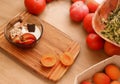A smoothie bowl with apricots placed on a wooden table. There are tomatoes and herbs around.