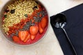 Smoothie bowl with blend fruits, strawberry, goji, chia seeds, and green buckwheat granola, and metal black spoon, on the table Royalty Free Stock Photo