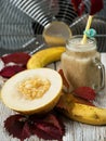 Smoothie with melon and banana. Juicy half melon on a wooden table next to bananas. Decorated with autumn leaves. Melon variety Royalty Free Stock Photo