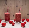 Smoothie of strawberries and berries in glass jars with beautiful tubes on a white wooden table, around expanded fresh strawbe Royalty Free Stock Photo