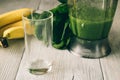 Smoothies in a food processor, glass, banana and spinach on a white wooden background