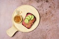 Smorrebrod on rye bread with beetroot mousse, pickled herring, fresh cucumber slices and crispy onion on a ceramic board on a Royalty Free Stock Photo