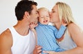 Smothering him with kisses. Two loving parents kissing their son on his cheeks while he looks upset and tries to push Royalty Free Stock Photo