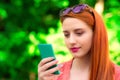 Sms. Smiling red head girl young woman texting video chatting talking looking at mobile phone profile view. In the park, outdoors Royalty Free Stock Photo