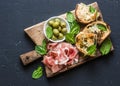 Snack board - prosciutto, olives, grilled mozzarella spinach sandwiches on dark background, top view. Mediterranean style snack, a Royalty Free Stock Photo