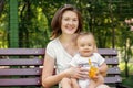 Snack break outdoor: happy mother and little infant child sitting on bench in the park. Face of kid is a little stained with food Royalty Free Stock Photo