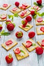 Snack: crackers with cream cheese, fresh strawberries and mint leaves on light wooden background