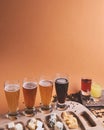 Snack platter with different cheeses with different kinds of cold beer on a bright orange or brown background.