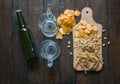 Snacks to beer, on a wooden board and two empty mugs,on a wooden table . Chips, peanuts, pieces of fish,crackers, bottle of beer. Royalty Free Stock Photo