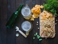 Snacks to beer, on a wooden board and two mugs of beer, on a wooden table. Chips, peanuts, pieces of fish,crackers, dill, bottle.