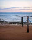 Snady beach woth wooden poles by the blue sea with sunset sky on the horizon Royalty Free Stock Photo