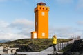 SNAEFELLSNES,Woman in yellow raincoat taking picture of Svortuloft Lighthouse, Snaefellsnes peninsula, Iceland